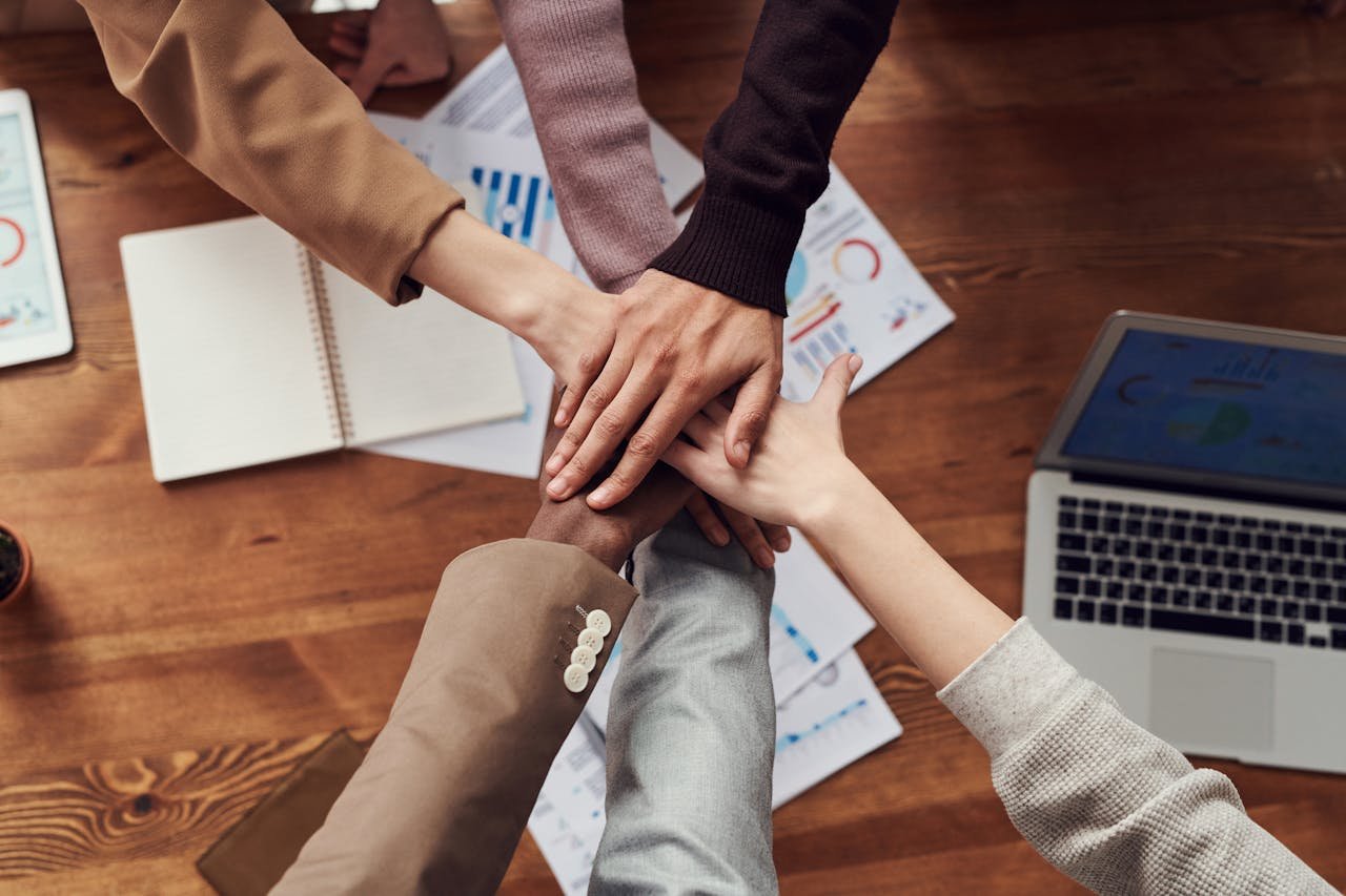 About Diverse professionals unite for teamwork around a wooden table with laptops and documents.