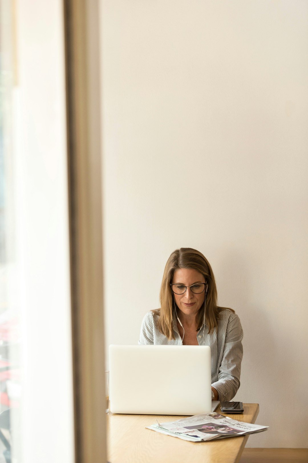 woman-wearing-grey-striped-dress-shirt-sitting-down-near-brown-wooden-table-in-front-of-white-laptop-computer-ws73le0gnks
